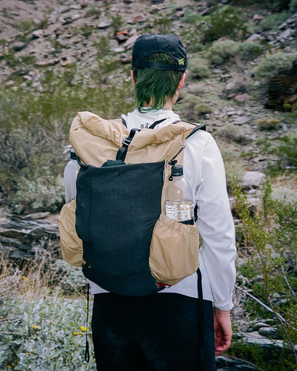 Hiker on a rocky desert trail wearing a Sweepeur roll-top pack